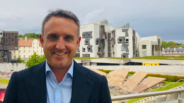 Alex standing outside the Scottish Parliament on a sunny day
