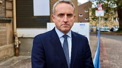 Alex Cole Hamilton standing in front of an NHS sign