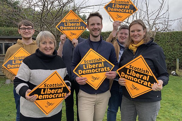 A group of activists standing behind Michael Andersen holding Lib Dem posters outside