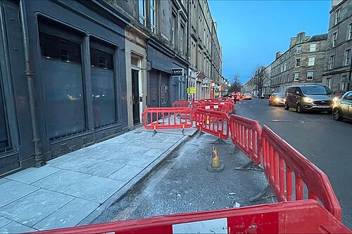 Barriers and a new pavement in the foreground of Albert Place during dusk