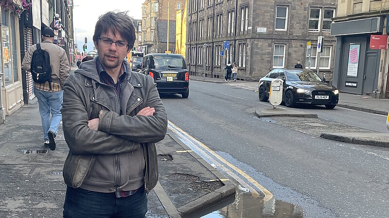 Councillor Jack Caldwell standing on a pavement on Easter Road with cars behind him