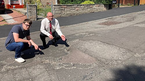 Cllrs Aldridge and Thornley pointing at a pothole on Clermiston Crescent