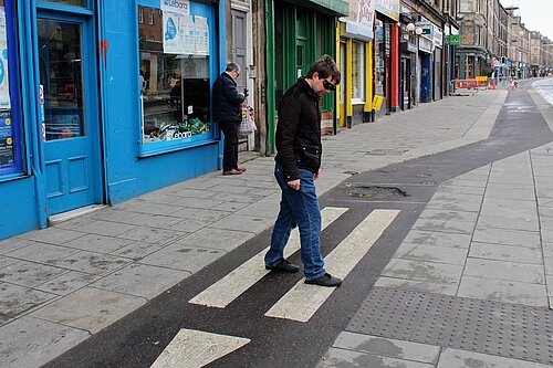 Man crossing a cycle lane with blind glasses on