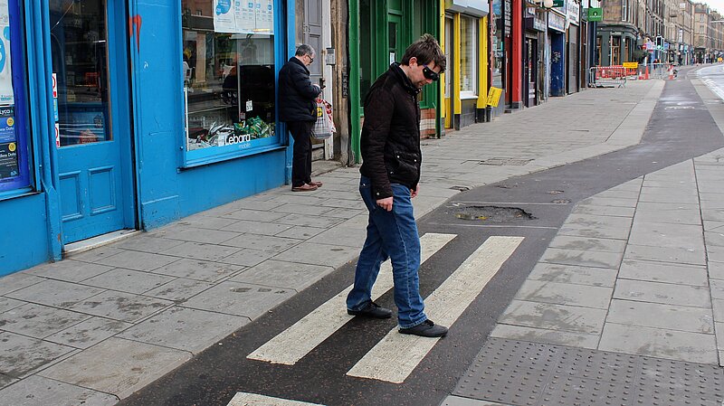 Man crossing a cycle lane with blind glasses on