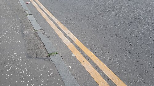 A set of double yellow lines running alongside a kerb on a grey road.