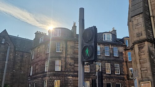 A Green Man signal at Pilrig Street with the sun and tenements in the background