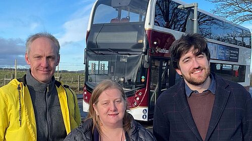 Three people standing in front of a bus