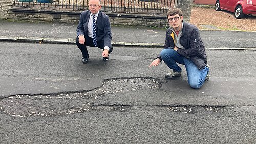 Cllrs Thornley and Aldridge pointing at a pothole on Parkgrove Drive
