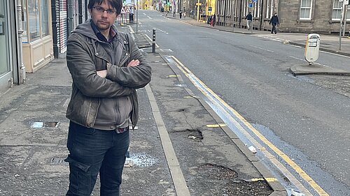 A man standing on a pavement on Easter Road