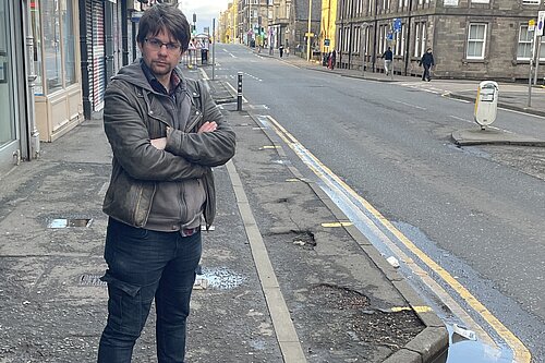 A man standing on a pavement on Easter Road