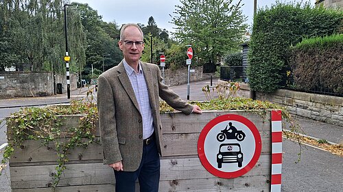 Councillor Neil Ross standing next to a "no cars and no motorbikes" sign on a planter