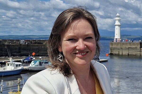 Sanne standing at Newhaven Harbour with blue skies, boats, and a lighthouse in the background